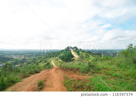 A dirt path winds up a green hill, flanked by trees and greenery under a cloudy sky, with a view of the horizon. Mondulkiri, Cambodia 116397374