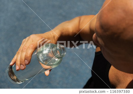 Athletes man drinking water on outdoor sports ground. Concept water balance for hot season for active workout and training. Close up. 116397380