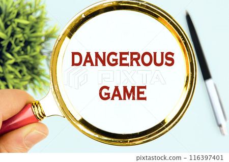 DANGEROUS GAME words through a magnifying glass in his hand on a white surface 116397401