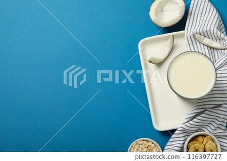 Glass of milk, towel, coconut and sliced bananas on blue background, space for text 116397727