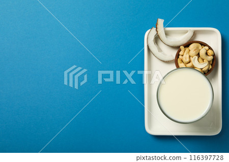 Glass of alternative milk, coconut and nuts in bowl on blue background, space for text 116397728