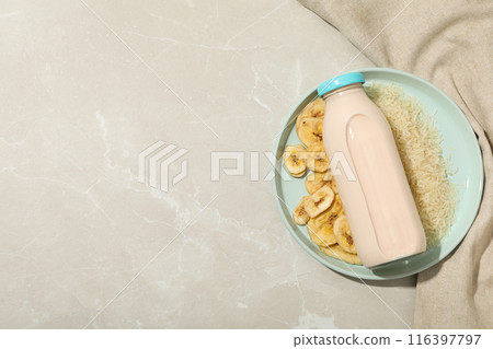 Bottle with milk on plate with rice and sliced bananas, towel on beige background, space for text 116397797