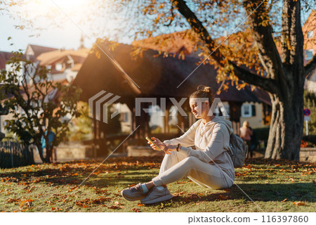 Young Fashionable Teenage Girl With Smartphone In Europian Park In Autumn Sitting At Smiling. Trendy Young Woman In Fall In Park Texting. Retouched, Vibrant Colors. Beautiful Blonde Teenage Girl Young Fashionable Teenage Girl With Smartphone In Europian Park In Autumn Sitting At Smiling. Trendy Young Woman In Fall In Park Texting. Retouched, Vibrant Colors. Beautiful Blonde Teenage Girl 116397860