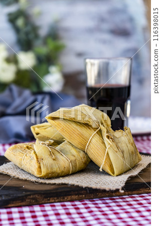 Traditional Andean corn and meat tamales served on a wooden board on a still life table with a glass of wine. Regional food. copy space. Traditional Andean corn and meat tamales served on a wooden board on a still life table with a glass of wine. Regional food. copy space. 116398015