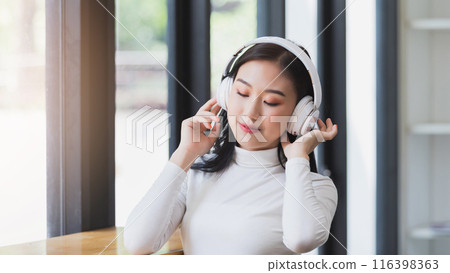 Asian woman wearing headphones listening to music and rocking to the rhythm of the music. Relaxing time. Asian woman wearing headphones listening to music and rocking to the rhythm of the music. Relaxing time. 116398363