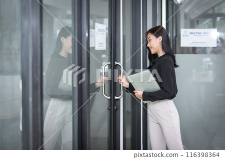 Young businesswoman with laptop opening meeting room door. Young businesswoman with laptop opening meeting room door. 116398364