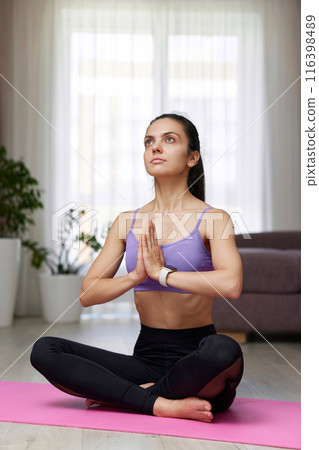 Caucasian woman practicing yoga and meditation sitting in lotus pose on pink yoga mat at home Caucasian woman practicing yoga and meditation sitting in lotus pose on pink yoga mat at home 116398489