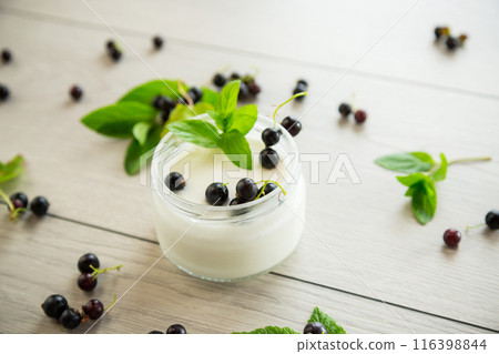 homemade sweet yogurt in a jar with black currants, on a wooden table 116398844