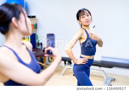 年輕女性在健身房、私人健身房、肌肉訓練女孩、私人房間用智慧型手機拍照 年輕女性在健身房、私人健身房、肌肉訓練女孩、私人房間用智慧型手機拍照 116400917