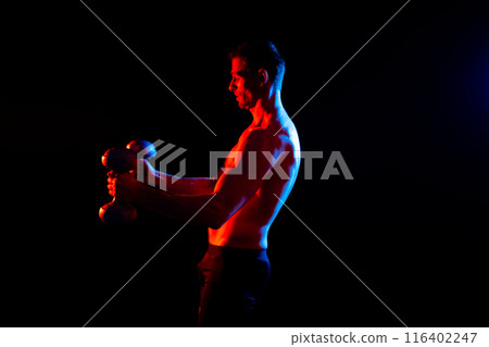 Bodybuilder exercising with dumbbells. Topless young man working out on studio background. 116402247
