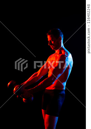 Bodybuilder exercising with dumbbells. Topless young man working out on studio background. 116402248
