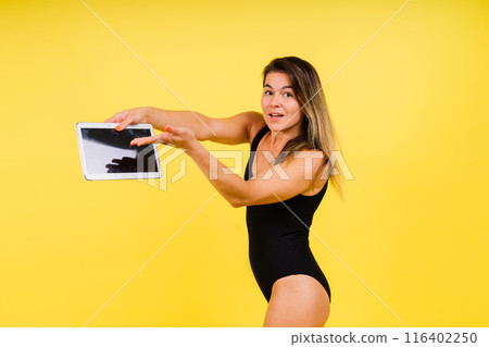 Female dressed in a bodysuit on a yellow background in studio with tablet laptop 116402250