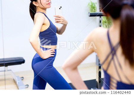 年輕女子在健身房、私人健身房、肌肉訓練女孩、私人房間用智慧型手機拍攝背部照片 116402440