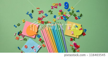 Stationery laid out on a green background. Multi-colored pencils ,  sticky notes and wooden letters, preparing for study or work 116403545