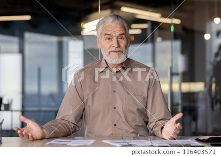Senior man seated in modern office environment discussing business plans. Expressive gestures and confident demeanor indicate engaged conversation. Senior man seated in modern office environment discussing business plans. Expressive gestures and confident demeanor indicate engaged conversation. 116403571