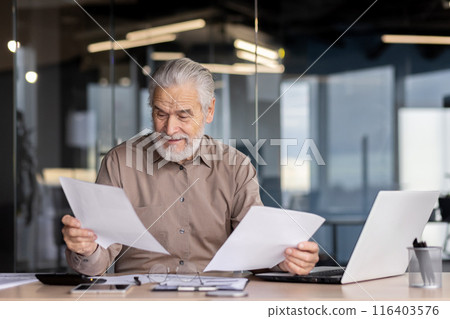 Senior businessman thoughtfully reviewing documents at modern office desk with laptop in a contemporary office setting. Concept of business, management, paperwork, decision making. Senior businessman thoughtfully reviewing documents at modern office desk with laptop in a contemporary office setting. Concept of business, management, paperwork, decision making. 116403576