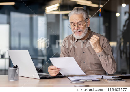 Senior businessman excitedly celebrating success while reviewing documents on laptop in modern office. Professional joyfully clenches fist celebrating achievement. Senior businessman excitedly celebrating success while reviewing documents on laptop in modern office. Professional joyfully clenches fist celebrating achievement. 116403577