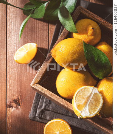 Fresh lemons with leaves in a wooden box on a dark board background close up. Fresh lemons with leaves in a wooden box on a dark board background close up. 116403837