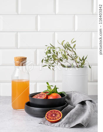 Freshly squeezed orange juice in a bottle on the kitchen table with fresh red oranges on plate.  116403842