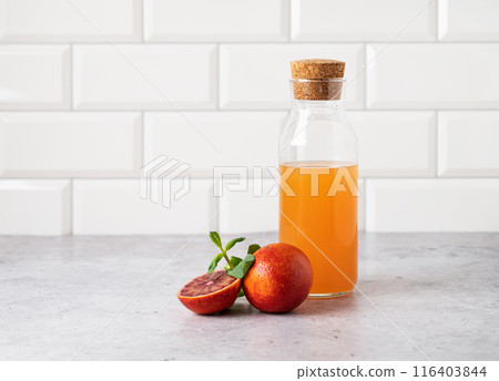 Freshly squeezed orange juice in a bottle on the kitchen table with fresh red oranges. Freshly squeezed orange juice in a bottle on the kitchen table with fresh red oranges. 116403844