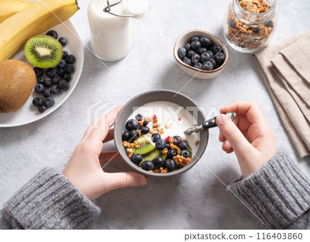 hands holding a bowl with a healthy breakfast of yogurt, granola and fresh  fruits kiwi, banana 116403860