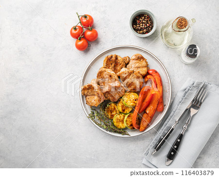 Grilled pork dish with fresh vegetables pepper and zucchini  in a plate on a blue background 116403879