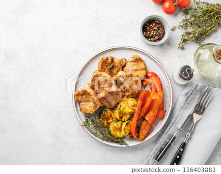 Grilled pork dish with fresh vegetables pepper and zucchini  in a plate on a blue background 116403881