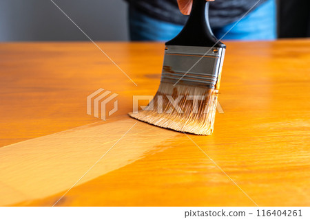 Painting table with brown enamel, brush in hand close-up, painting wood furniture process with brownish dye Painting table with brown enamel, brush in hand close-up, painting wood furniture process with brownish dye 116404261