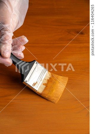 Painting table with brown enamel, brush in hand close-up, painting wood furniture process with brownish dye 116404265