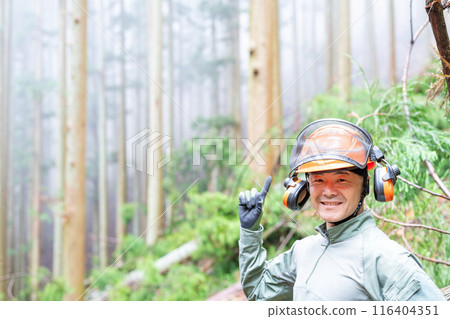 A man working in forestry raises his index finger in relief after safely completing his work and smiles, emphasizing "safety first." A man working in forestry raises his index finger in relief after safely completing his work and smiles, emphasizing "safety first." 116404351