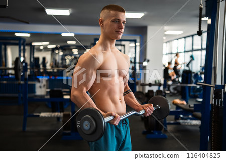 A muscular bodybuilder trains his biceps with a barbell in a gym A muscular bodybuilder trains his biceps with a barbell in a gym 116404825
