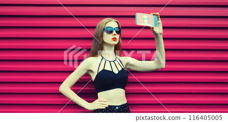 Stylish young woman taking selfie with smartphone, modern girl using phone in black, glasses on pink 116405005