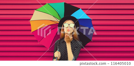 Autumn portrait of stylish woman model posing with colorful umbrella blowing kiss on pink background 116405010