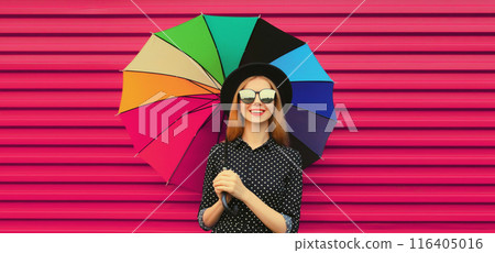 Portrait stylish happy smiling young woman holding colorful umbrella in glasses on pink background 116405016
