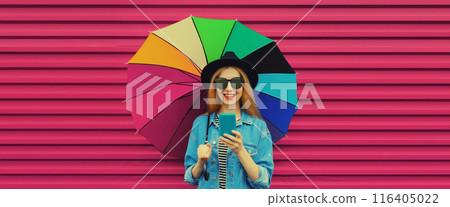 Joyful happy young woman looking at smartphone, cheerful girl smiles holding colorful umbrella 116405022