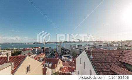 Panorama showing red roofs timelapse and 25 de Abril Bridge, Iconic suspension bridge over Tagus River in Lisbon, Portugal. 116405406