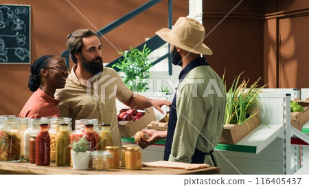 Vendor assists clients in grocery store, recommending freshly harvested fruits and veggies in crates. People searching for organic bio produce at local zero waste market, sustainable lifestyle. Vendor assists clients in grocery store, recommending freshly harvested fruits and veggies in crates. People searching for organic bio produce at local zero waste market, sustainable lifestyle. 116405437