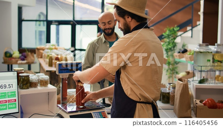 Man checking weight of produce using modern market scale and selling fresh items to customer. Local grocery store vendor weighting potatoes and pasta in reusable container. Handheld shot. 116405456