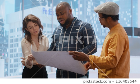 Entrepreneur evaluating an investment opportunity in real estate, reviewing blueprints on tablet and discussing the architectural plans of the new office space with the realtor agent. Camera B. 116405544