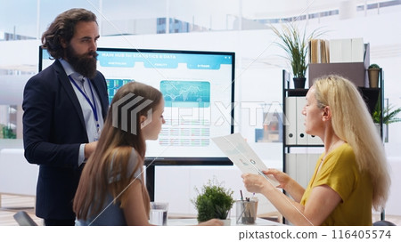 Financial advisor discussing with clients, recommending suitable financial products such as mutual funds. Agent teaching parent and daughter how to invest, offering statistical graphs, camera B 116405574