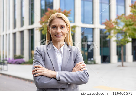 Portrait of confident businesswoman standing with arms crossed outdoors. Female professional in suit standing in front of modern office building. Concept of leadership, success, and career. Portrait of confident businesswoman standing with arms crossed outdoors. Female professional in suit standing in front of modern office building. Concept of leadership, success, and career. 116405575