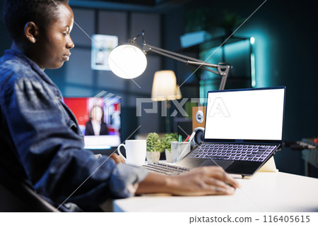Female freelancer focused and utilizing technology while working at home with digital laptop having isolated white screen. Black woman looking at personal computer displaying blank mockup template. 116405615