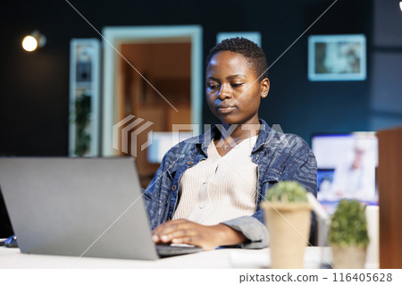 Focused college student working on her thesis, using a laptop for researching, and reviewing information online. Dedicated and determined, black woman working from home on personal computer. Focused college student working on her thesis, using a laptop for researching, and reviewing information online. Dedicated and determined, black woman working from home on personal computer. 116405628