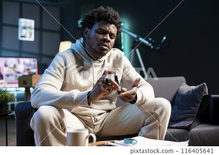 African american man clipping own finger using pulse oximeter, monitoring level of blood oxygen saturation and heart rate during annual checkup from comfort of his dimly lit home African american man clipping own finger using pulse oximeter, monitoring level of blood oxygen saturation and heart rate during annual checkup from comfort of his dimly lit home 116405641