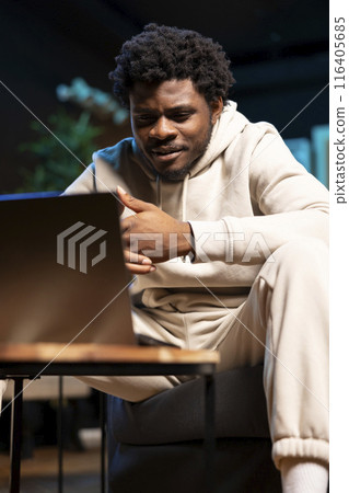 BIPOC remote employee sitting at home on couch late at night in front of laptop, overthinking problems. Man struggling to finish job tasks before deadline, trying to come up with solutions 116405685
