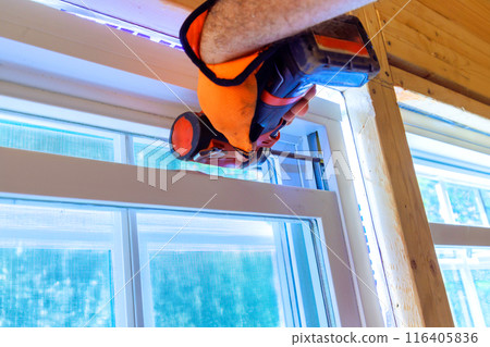 Construction worker installs window in new house is uses screwdriver 116405836