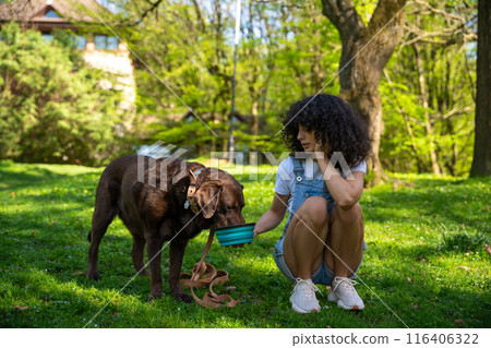 Dog owner giving water to her pet in the park 116406322
