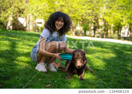 Dog owner giving water to her pet in the park 116406329