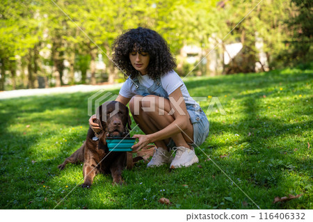 Dog owner giving water to her pet in the park Dog owner giving water to her pet in the park 116406332