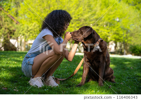 Curly-haired young woman playing with her dog in the park Curly-haired young woman playing with her dog in the park 116406343